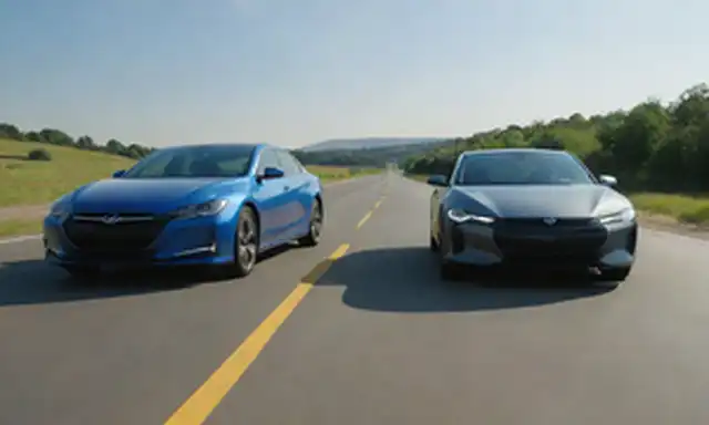 2 coches lado a lado, un híbrido eléctrico y uno totalmente eléctrico, con cables de carga o enchufes en el fondo, carretera soleada por delante