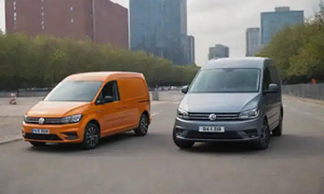 2022 VW Caddy and Transporter electric vans, lado a lado en un día soleado, con un vehículo que tiene sus puertas abiertas, mostrando espacio interior, ambos vehículos estacionados cerca de un moderno paisaje urbano o entorno industrial, posiblemente con una estación de carga en el fondo, con líneas limpias, acentos de iluminación LED, y diseños aerodinámicos