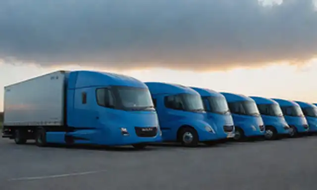 250-350 camiones eléctricos estacionados en filas, cielos azules brillantes con un toque de amanecer, fondo futurista de paisaje urbano, camiones luces LED brillantes, logotipo de Nikolas en la parte trasera del camión, nubes sutiles y niebla