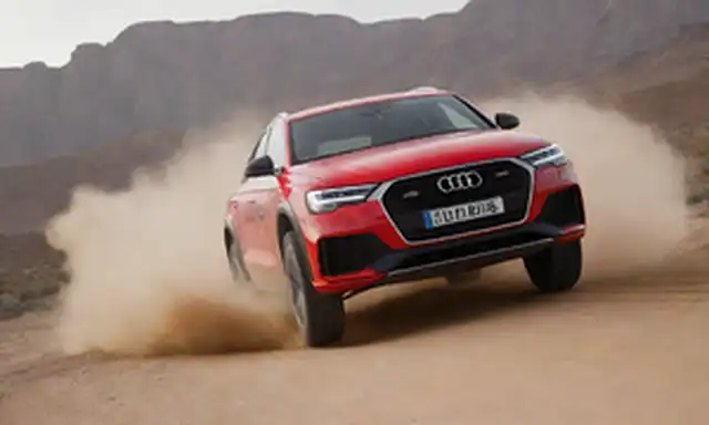 4x4 coche acelerando a través del paisaje del desierto, sol golpeando, arena volando fuera de ruedas, Carlos Sainz y Lucas Cruz en asiento de conductores, Audi RS Q e-tron modelo destacado, e-tron logotipo eléctrico prominente, terreno robusto en el fondo, emoción y acción