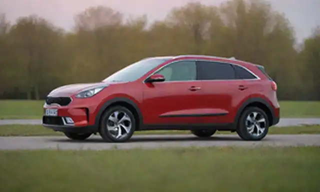 2023 Kia Vehículo eléctrico híbrido Niro en un ambiente tranquilo y natural, como un parque o prado, con una paleta de color sereno, con un ángulo frontal que muestra el diseño elegante y la forma aerodinámica de los coches, en un fondo suave y cálido, destacando sus características ecológicas