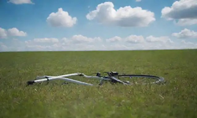 Una bicicleta, con un cable de carga enchufado, sentado en una superficie verde de hierba, bajo un cielo azul brillante con nubes blancas suaves, en medio de un gradiente de fondo sutil