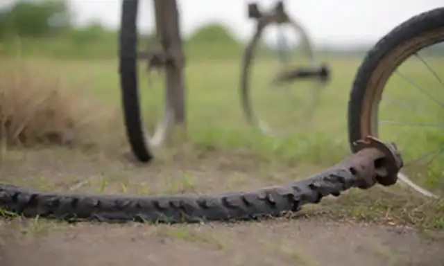 un disparo de cerca de una bicicleta con un neumático desgastado, una cadena oxidada y un motor sucio, sentado en una superficie pastosa, bajo un cielo soleado, con un fondo borroso sutil