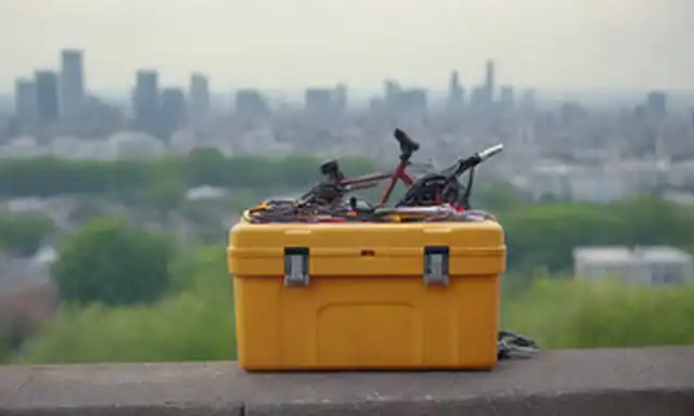bicicleta con una caja de herramientas, llave en mano, rodeada de componentes eléctricos como alambres, motores y baterías, con un fondo borroso de un paisaje urbano o escena natural, incorporando tonos terrenales y colores vibrantes