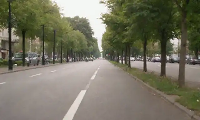 Scooters eléctricos en una calle de la ciudad con vegetación, cielo soleado, gente caminando o de pie cerca, árboles pequeños, flores, carriles de bicicleta, signos de tráfico, arquitectura urbana, pavimento, ruedas, movimiento borroso