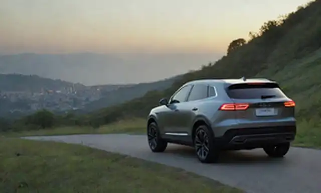 eléctrico de lujo de 7 pasajeros SUV en un diseño elegante, con faros LED y luces traseras brillando brillantemente, estacionado en una ladera escénica con vistas a un paisaje urbano al atardecer, rodeado de vegetación exuberante, con un efecto sutil gradiente para insinuar la tecnología avanzada
