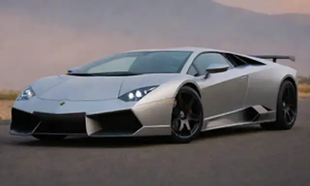 2023 Lamborghini Reventón coche deportivo híbrido, diseño elegante, líneas angulares, brillante trabajo de pintura plateada, rejilla frontal agresiva, tomas de aire prominentes, spoiler trasero masivo, puertas tijeras, cuatro faros LED circulares, dos tubos de escape, neumáticos con patrón de pisada intrincado, pose dinámica en una superficie lisa