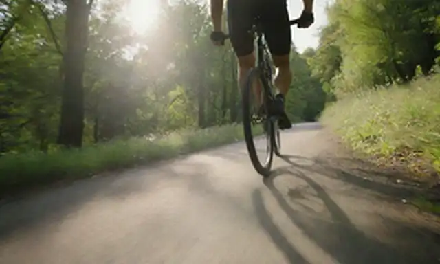 Una persona montando una bicicleta elegante y moderna en un sendero pintoresco con vegetación exuberante, las piernas de los jinetes bombeando suavemente mientras navegan por una suave colina, la luz del sol arrojando largas sombras detrás de ellas, un fondo sutil que transmite movimiento y libertad
