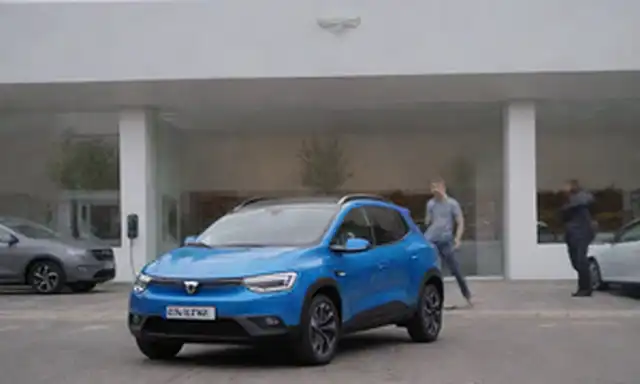 2023 Coche eléctrico Dacia frente a una tienda de Tesla, paisaje urbano con índice de calidad del aire que reduce la contaminación, estación de carga en el fondo, gente sonriente con aparatos futuristas, fuentes de energía ecológicas y modos de transporte sostenibles