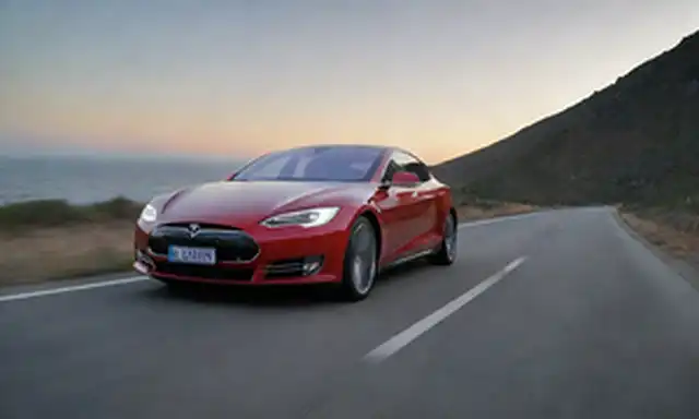 A Tesla Model Conduciendo en una carretera española, con neumáticos Tempest, al atardecer, en una región costera o montañosa, con un largo tramo de carretera, con un tráfico mínimo, y un cielo claro con algunas nubes, sin señales de obstáculos ni peligros, mostrando los coches Autopilot sistema